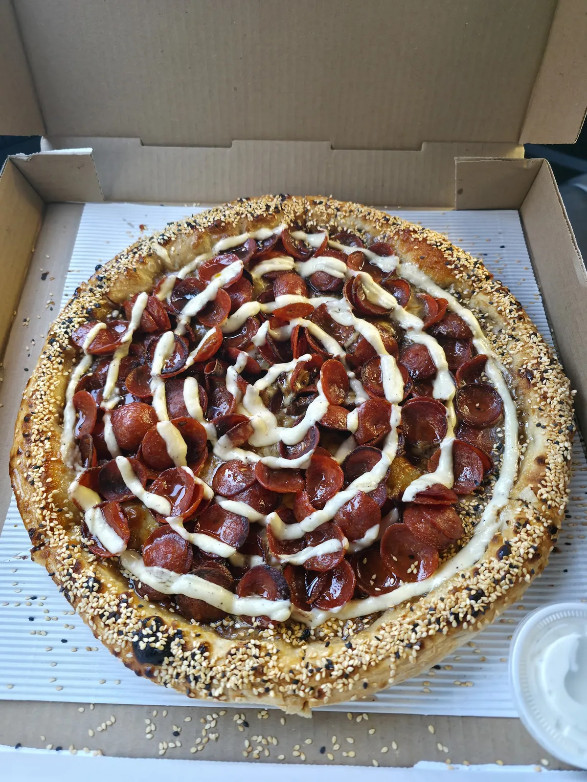 Pepperoni pizza with white sauce drizzle in a pizza box